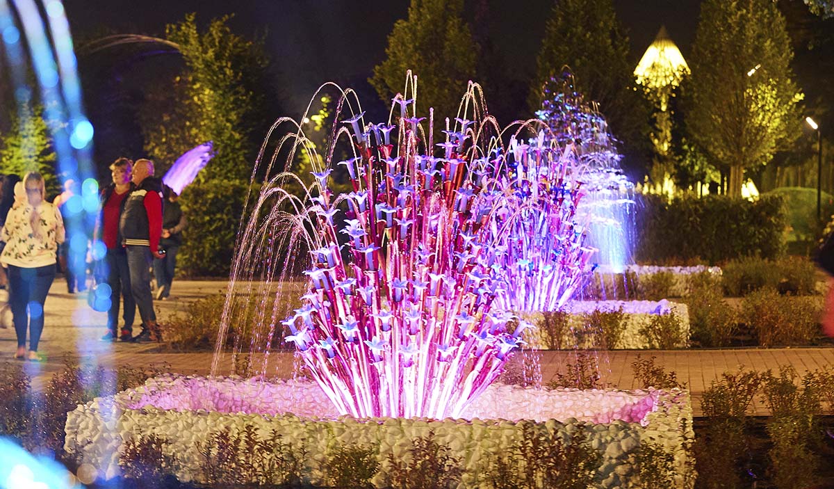 Public art with backlighting and decorative glass flower elements on a city alley at night